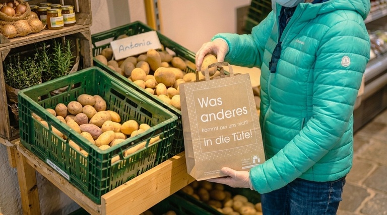 Papiertragetasche wird von Kundin mit Kartoffeln befüllt